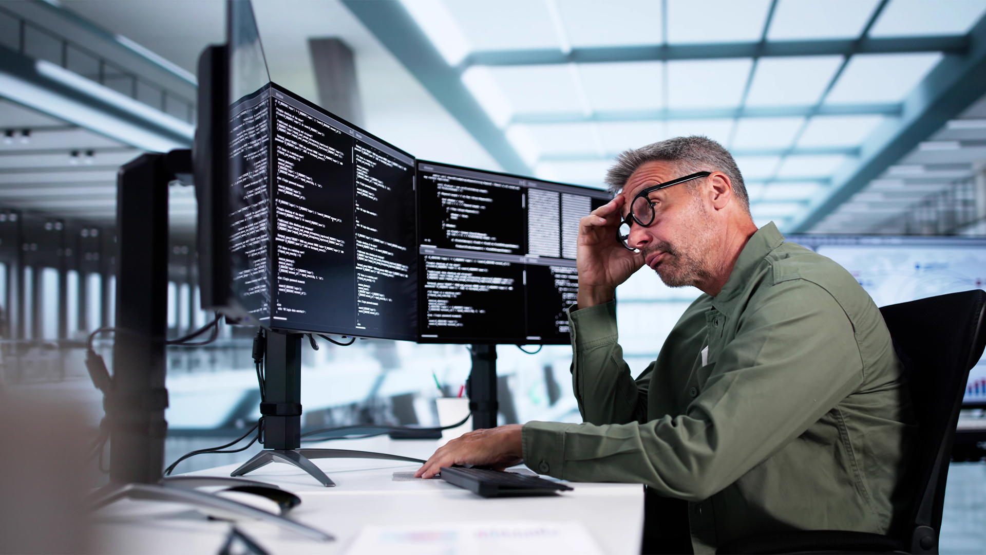 Male office worker sitting at desk looking frustrated and burned out while working with software application.