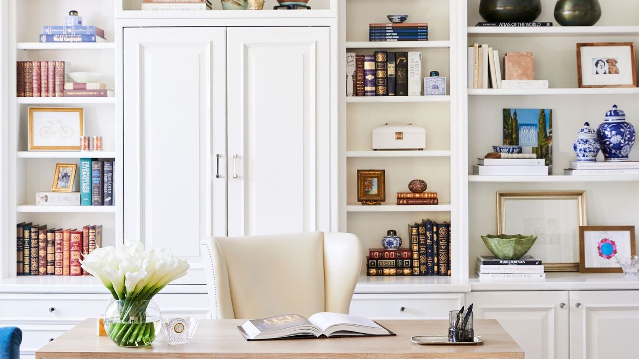 A whote home office with built in shelving and a wooden desk, books and trinkets adornding the shelves 