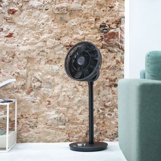 black pedestal fan in living space with exposed brick wall and sofa