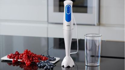 Braun immersion blender in white on a countertop with a blending cup and some fruit beside it