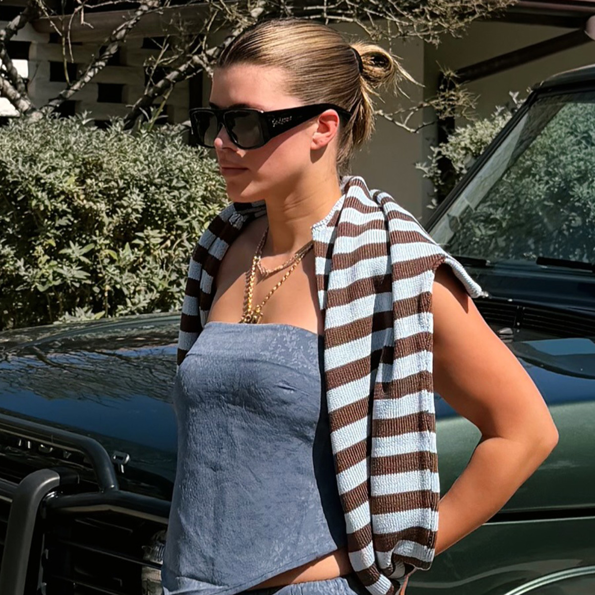 Sofia richie wears sunglasses, a blue strapless top, and a stripe shirt.
