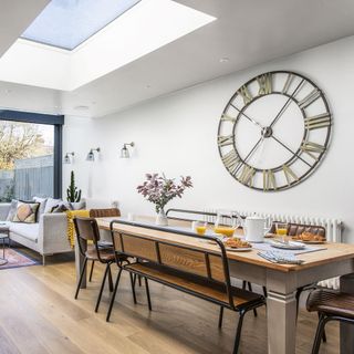 open kitchen with dining table and chairs with bench and clock on wall