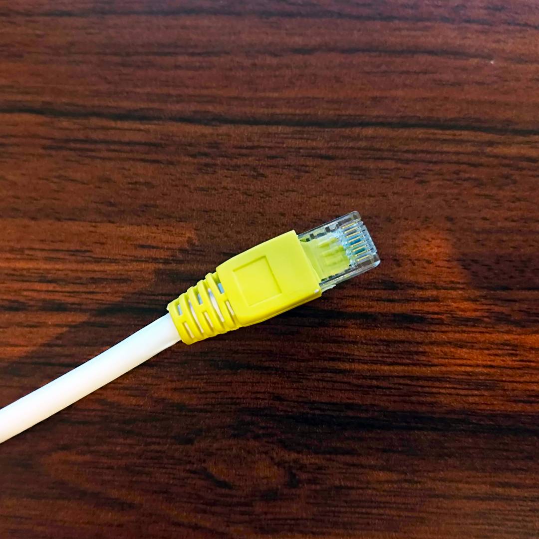Yellow Ethernet cable sitting on woodgrain desk.