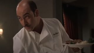 Artie Bucco wearing a chef coat and holding a plate of food in The Sopranos