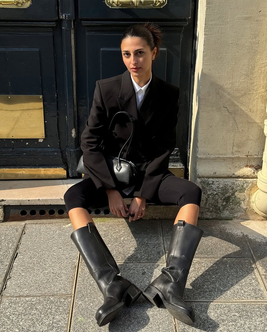 French influencer @salome.mory wears a black blazer with black capris and black knee-high pull-on boots.