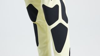 A close up of black abrasion-resistant patches on the knee of the pastel yellow trail pants