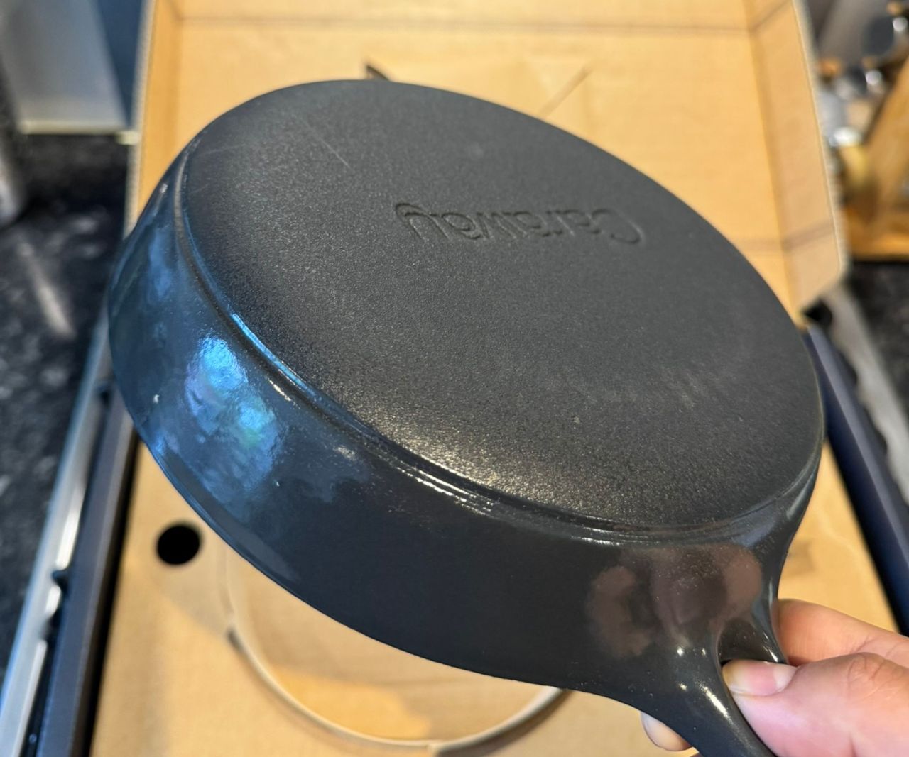 The rough base of the black cast iron mini skillet, being held over the box.