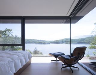 A minimalist bedroom with leather lounge chair a large windows with panoramic lake views