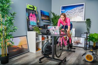 A rider trains indoors with a fan blasting, and a music speaker beside her