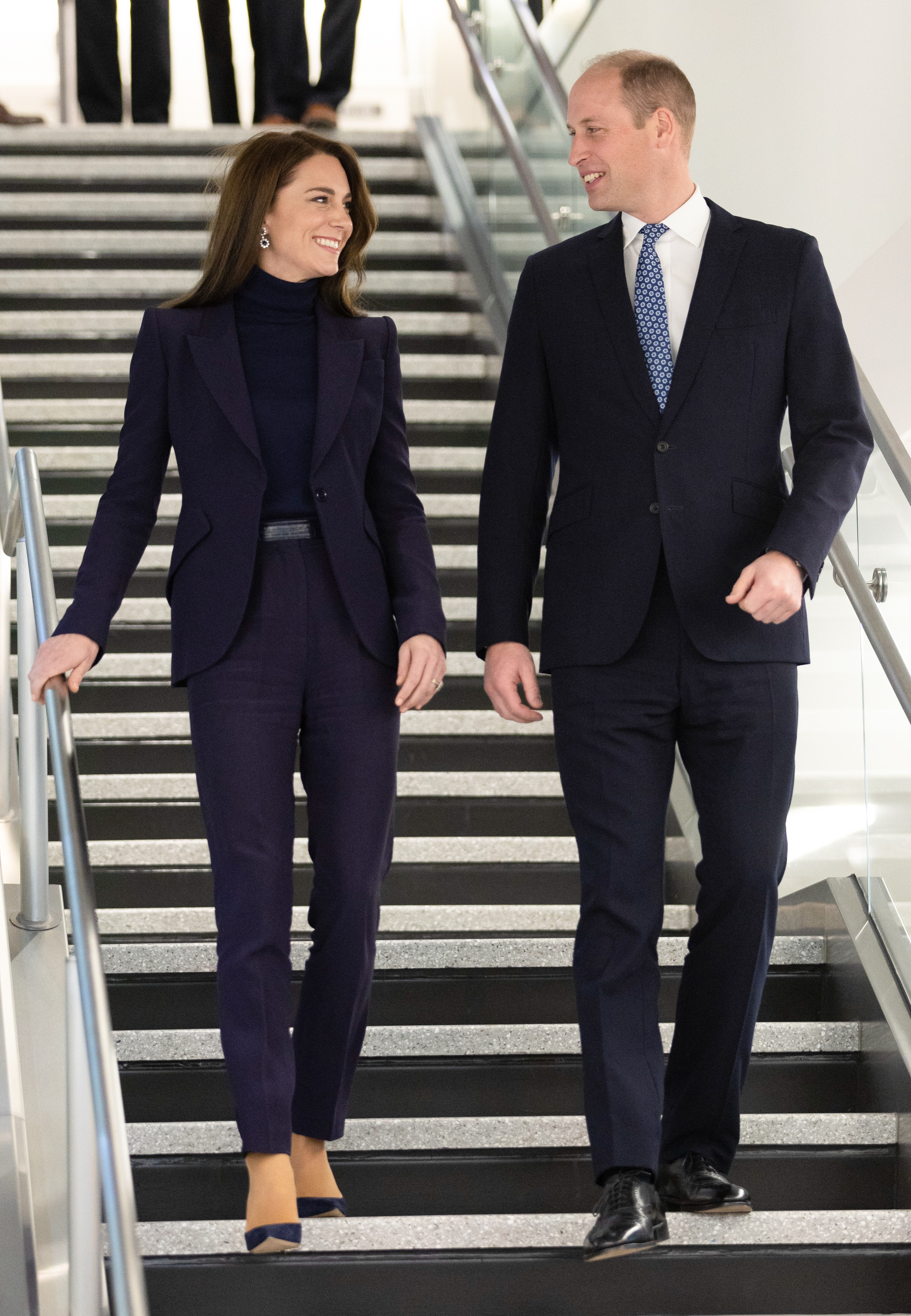 Prince William and Princess Kate walking down stairs in suits