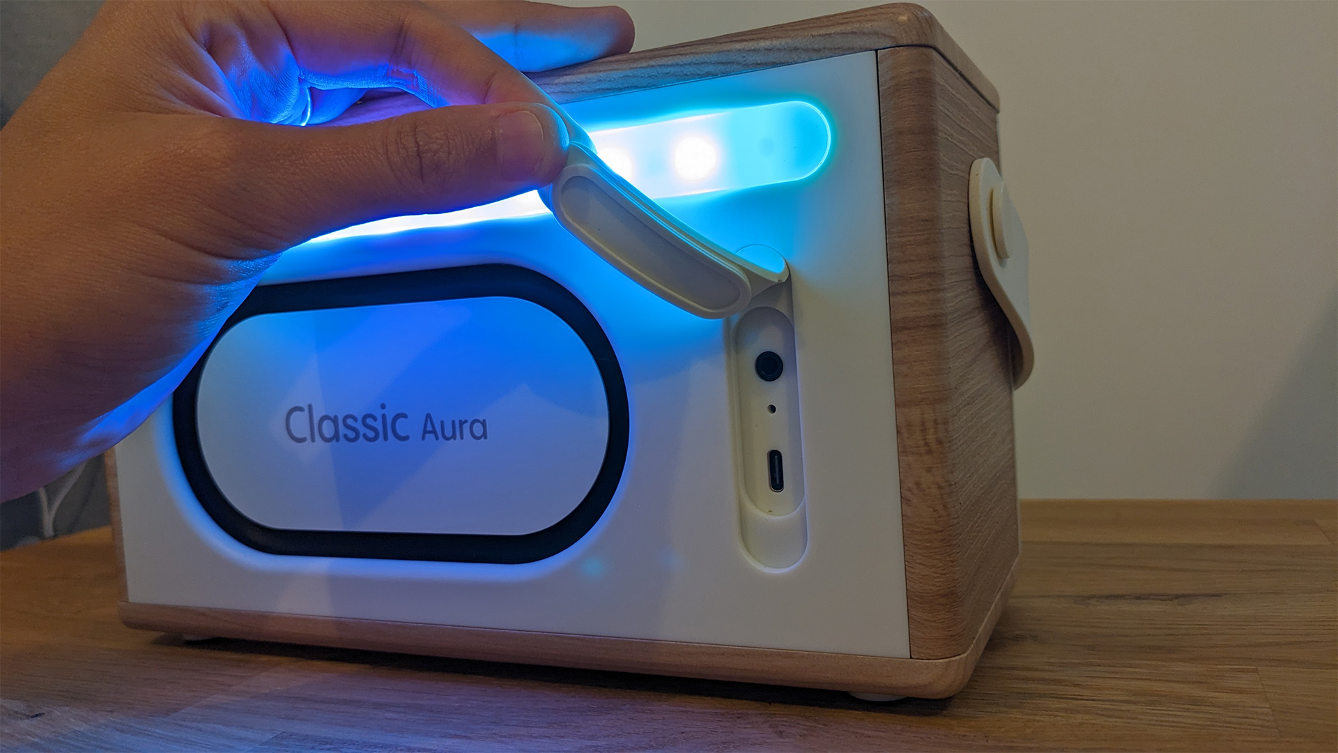 Pure Classic Aura Bluetooth speaker, back of speaker emitting blue light and with hand lifting flap to reveal connections