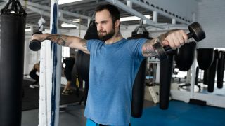 Man performs lateral raise shoulder exercise with dumbbells