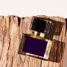 Bird's eye view of a perfume bottle with a dark navy label sat on a large piece of bark in front of a beige background - tobacco perfumes