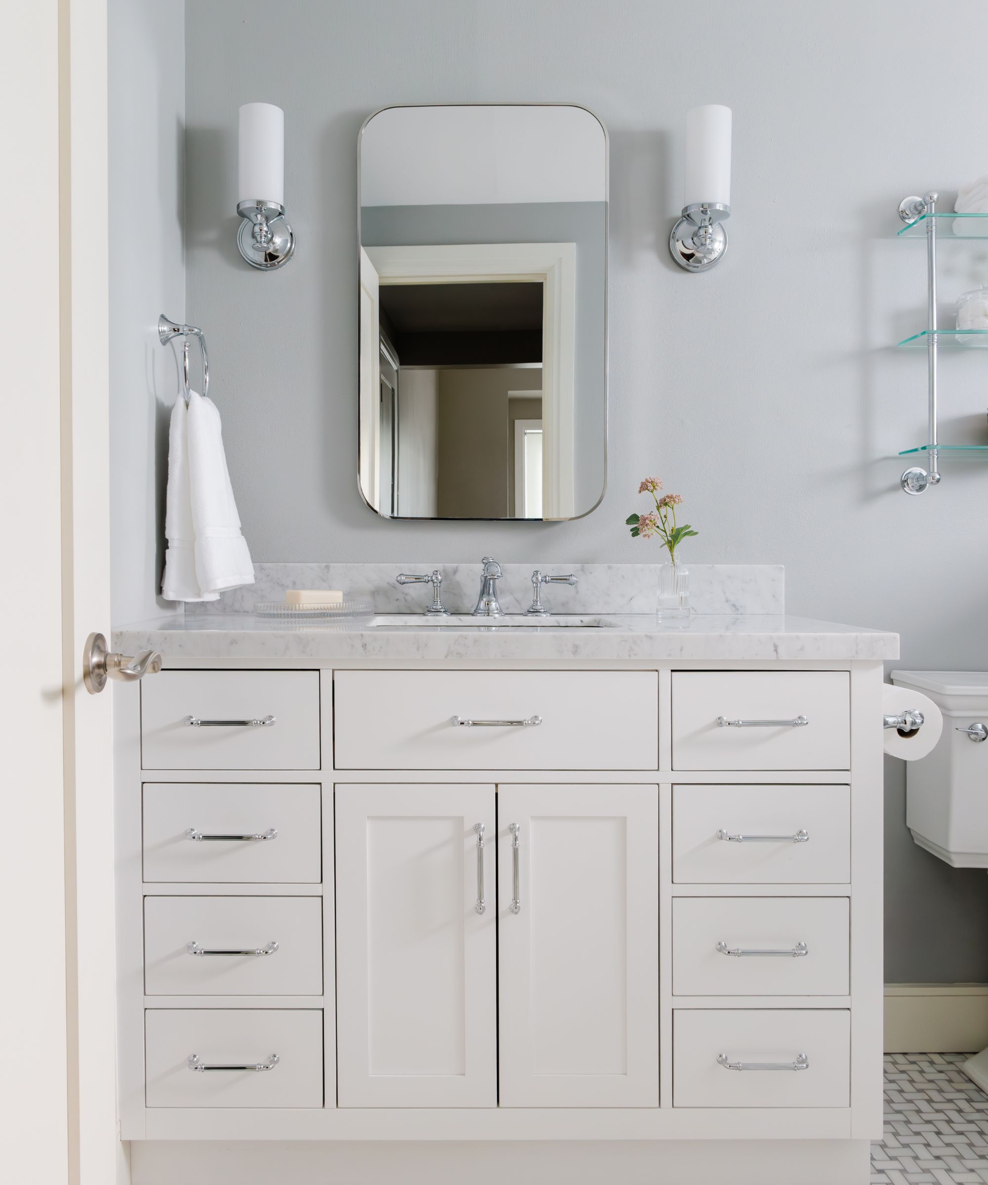 A traditional bathroom with blue-gray walls, a white vanity, chrome fixtures and a marble countertop.