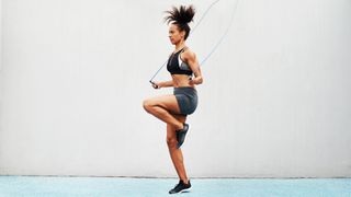 Woman jumping rope against white wall during jump rope HIIT workout