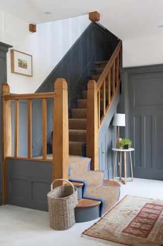 Hallway and staircase with red patterned rug and natural runner and blue paneling to dado height