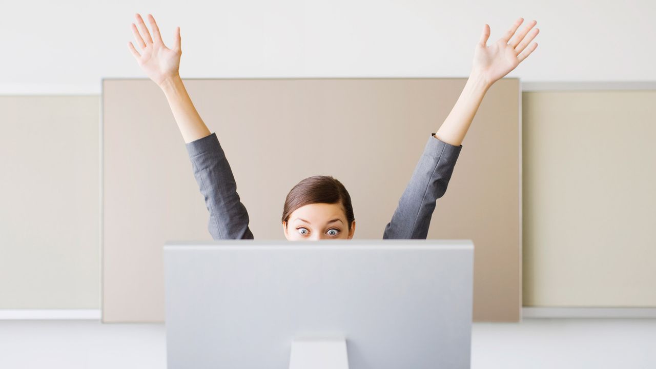 Woman throws up her hands in celebration at her workstation