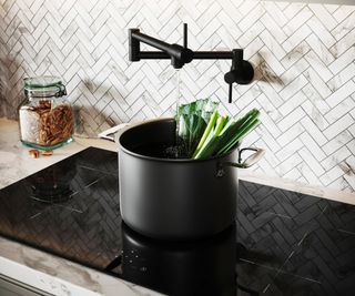 black pot filler on herringbone white tiled wall with large black pot on glass hob