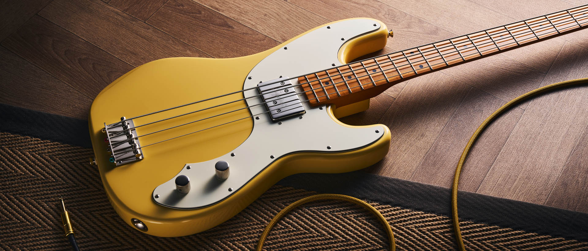 The Squier Classic Vibe Telecaster Bass is a fine-looking four-string in a custard-colored Vintage White, and is here photographed in close-up, against a plain wooden background. It has a single Wide Range humbucker.