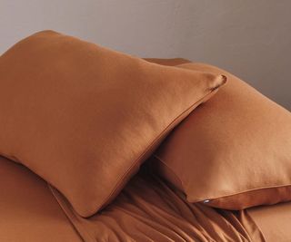 Shleep bedding in Rust against a gray background.