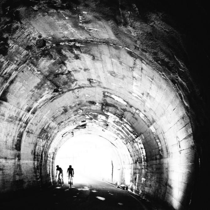 Two riders make their way through a mountain tunnel.