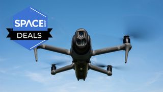 A black quadcopter is hovering in the air in front of clear blue skies with the Space.com logo in the top left corner.