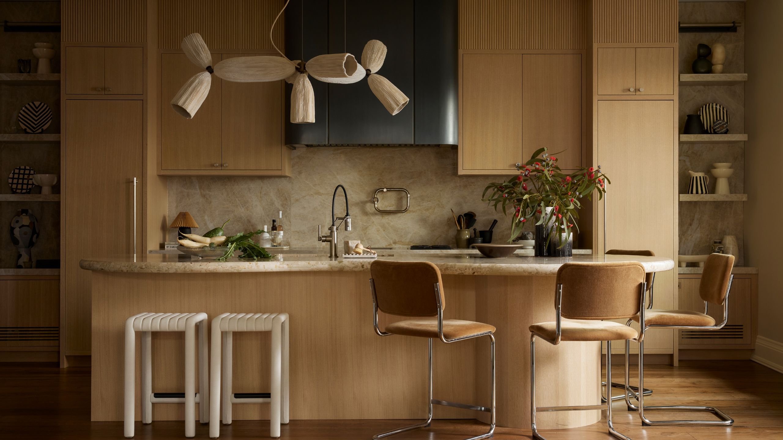 an oak wooden kitchen with contemporary flat front cabinetry, curved island and sculptural pendant and stools