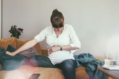 Expectant mother timing her contractions while sitting on couch at home