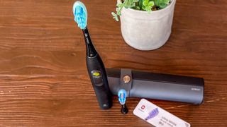 The Oclean X Ultra S toothbrush standing on a table beside its travel case and brush heads