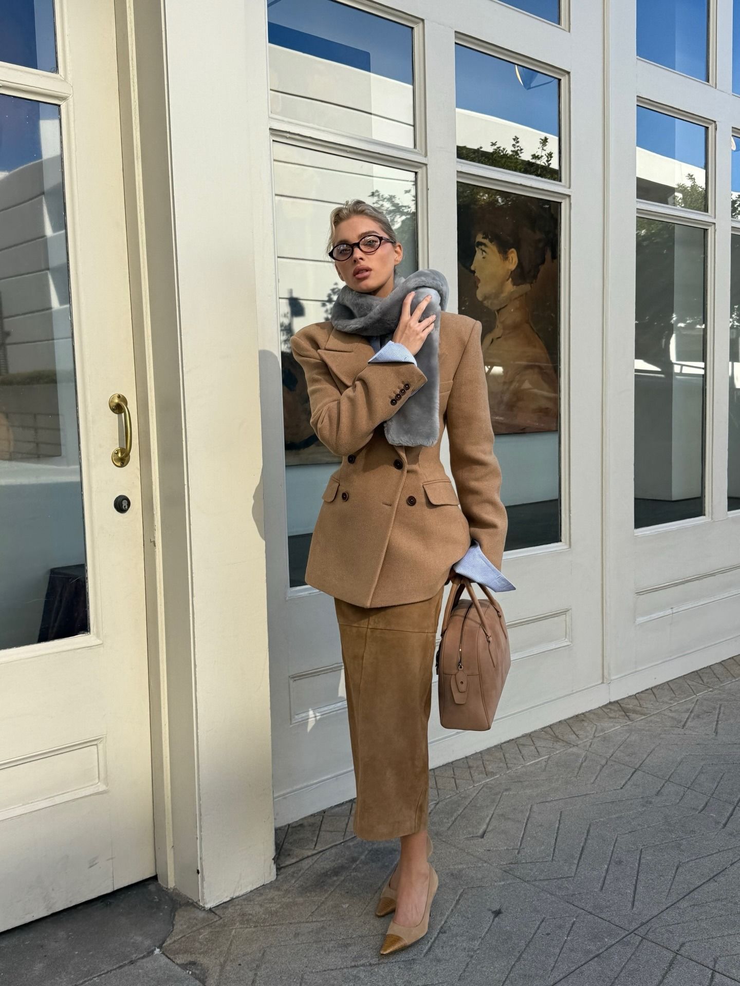 Elsa Hosk wearing a camel blazer and suede pencil skirt with pumps, a blue shirt, and a gray fur scarf
