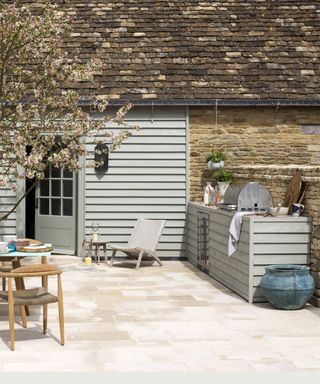 A classic pale gray wood scheme with stone pavers to illustrated how much does an outdoor kitchen cost.