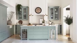 light duck egg blue kitchen from the Suffolk range by Neptune, white walls, kitchen island has matching cabinetry, white tiled floor, wall units with glass, clock, pendant lights