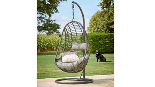 Cox & Cox Slim Black Hanging Chair with Base in a sunny garden with a dog in the background
