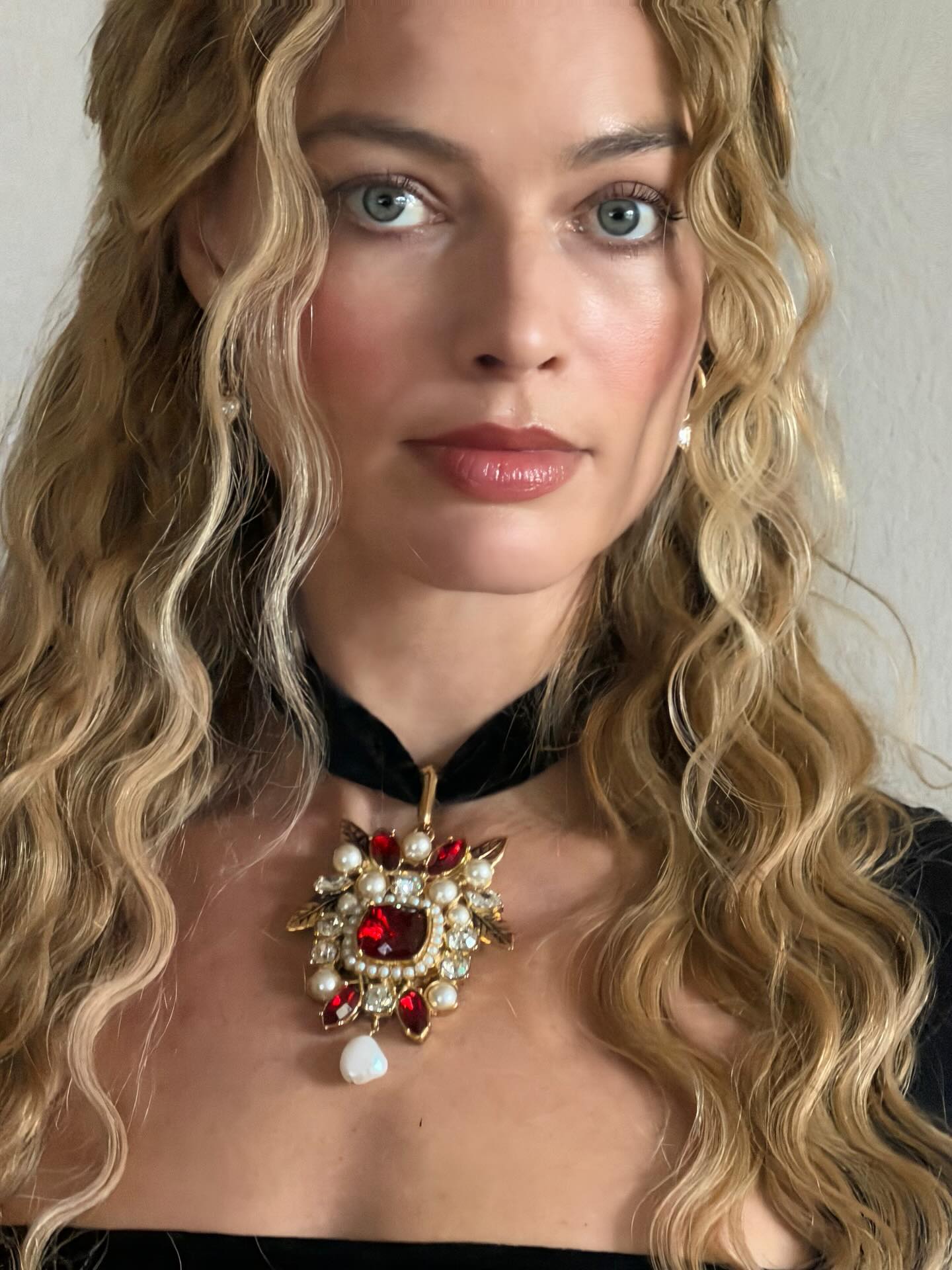 Margot Robbie looking directly to camera; a close-up of her hair and makeup with tumbling blonde S-waves