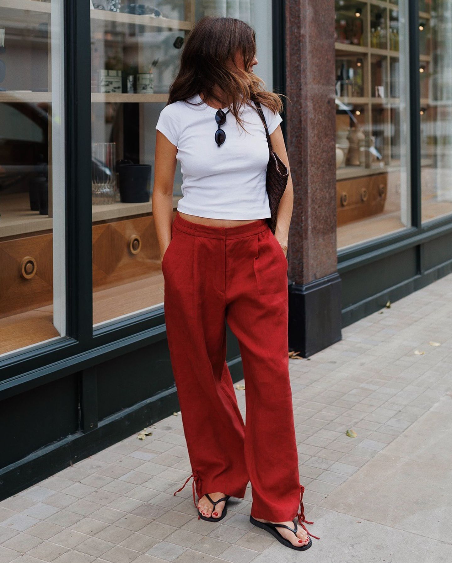 British style influencer Kim Turkington poses on a sidewalk wearing a white T-shirt, relaxed red pants, and black flip-flop sandals