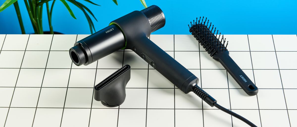 the heist 3.0 men&#039;s hair dryer in black with a bright green ring and magnetic attachment photographed against a blue background 