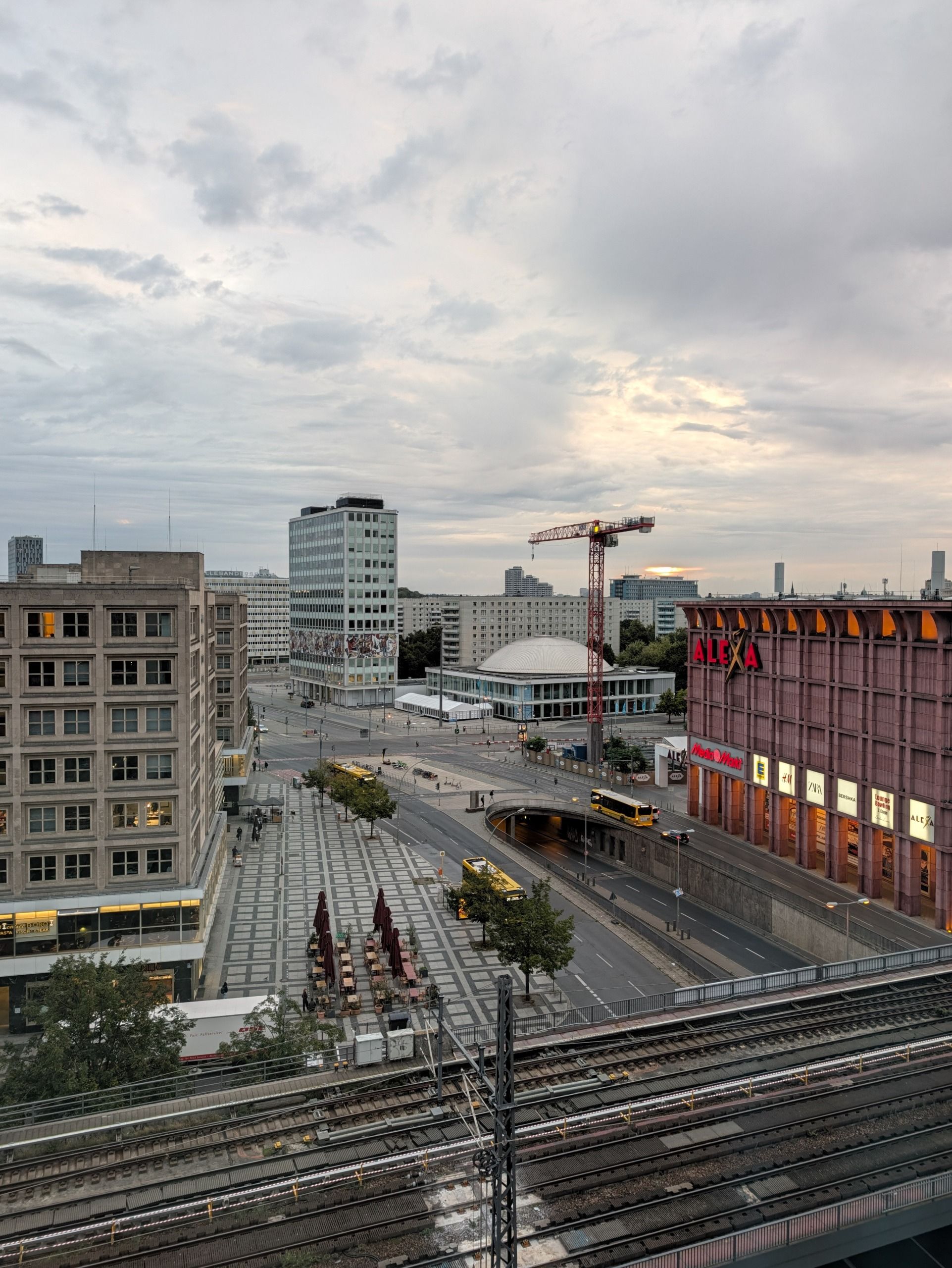 Elevated view across Berlin buildings, roads and railway tracks beneath an overcast evening sky.