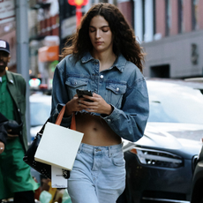 Women with small shopping bag wearing jean jacket and low-waisted jeans texting on iphone 