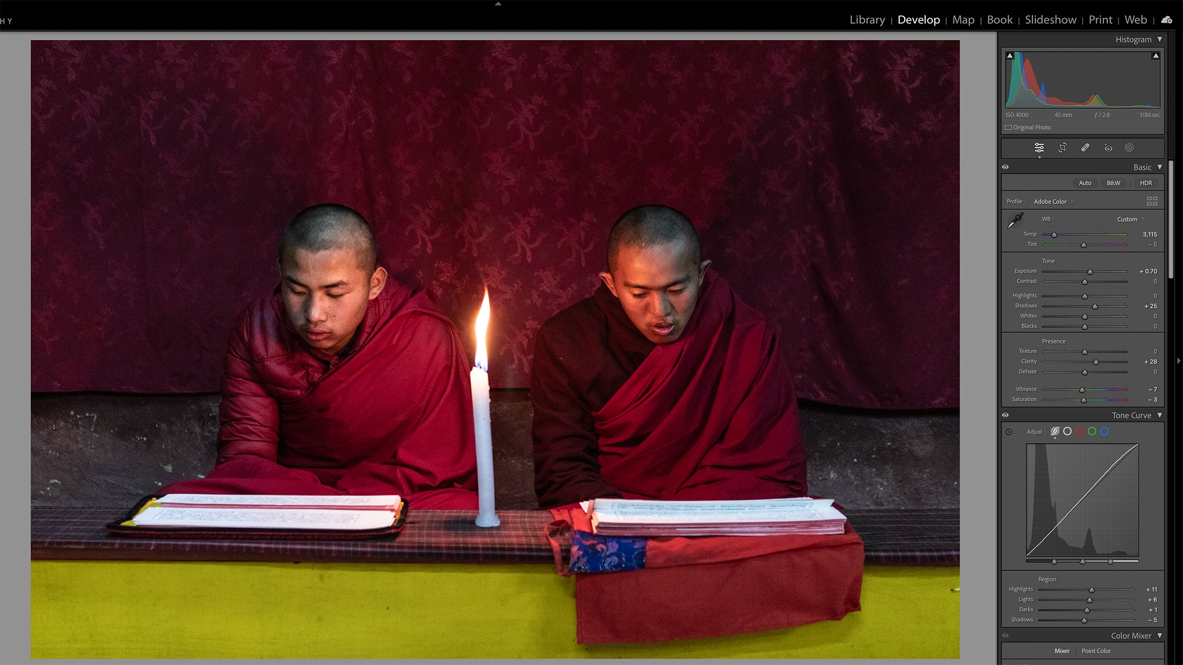 Two individuals in maroon robes are seated side by side, reading by candlelight. The dim setting conveys a calm and meditative atmosphere