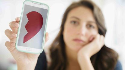 Photo of a woman holding a cell phone with an image of a broken heart