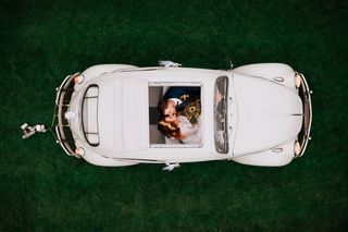 A recently married couple kissing in a vintage Volkswagen Beetle on a green background