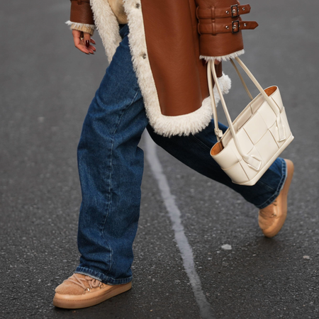 BERLIN, GERMANY - NOVEMBER 25: Laura Noltemeyer is seen wearing a shearling lining coat in a rich cognac tone with an oversized straight silhouette, wide lapels and buckle-strap cuff detailing on the sleeves from Max&Co; layered underneath is a soft beige wool-blend knit sweater with a ribbed crew neckline and ribbed trims from S&eacute;zane; dark-blue straight-leg denim trousers with a classic fit from By Aylin Koenig; beige suede winter boots with a rounded toe, exposed stitching and shearling lining from Inuikii; a white structured leather top-handle bag in an intrecciato weave and trapeze silhouette called &ldquo;Intrecciato Tote&rdquo; from Bottega Veneta on November 25, 2025 in Berlin, Germany. (Photo by Moritz Scholz/Getty Images)