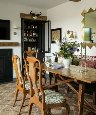 Rustic dining room with wooden chairs and table, fabric sofa, floral display and drinks cupboard