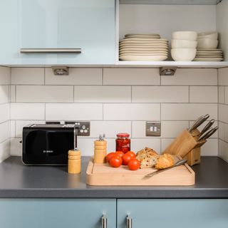 A kitchen counter with a toaster, block of knifes and a chopping board with veggies