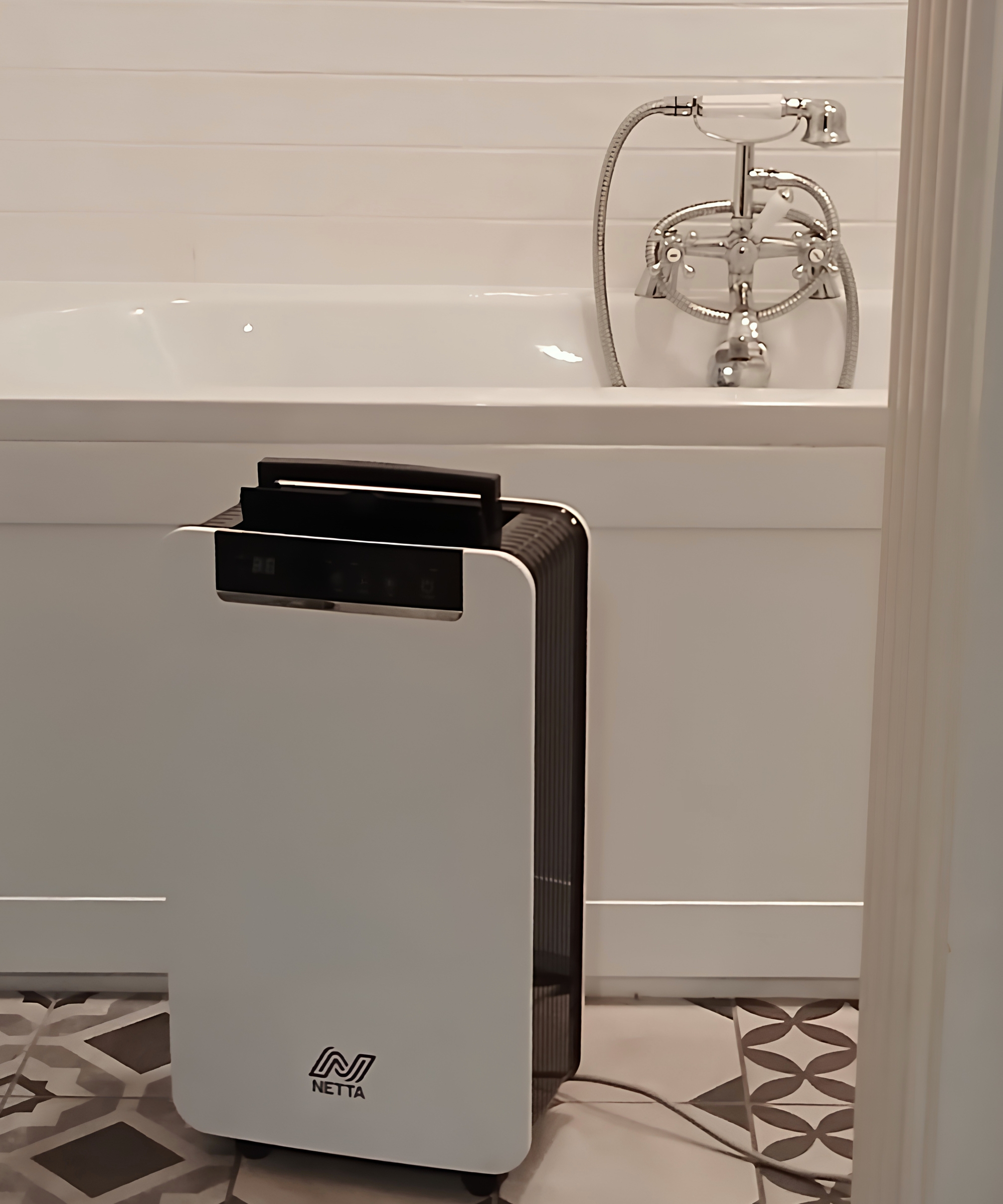 White and black Netta dehumidifier beside a white bath with chrome mixer tap and shower, on patterned floor tiles