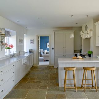 kitchen with white wall white counter white cabinets wooden bar stool and stone floor