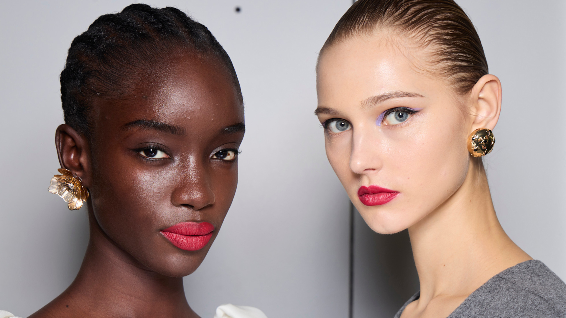 two models backstage at carolina herrera wearing red lipstick and winged eyeliner