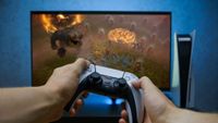 PS5 Dualsense held in front of a PS5 and monitor