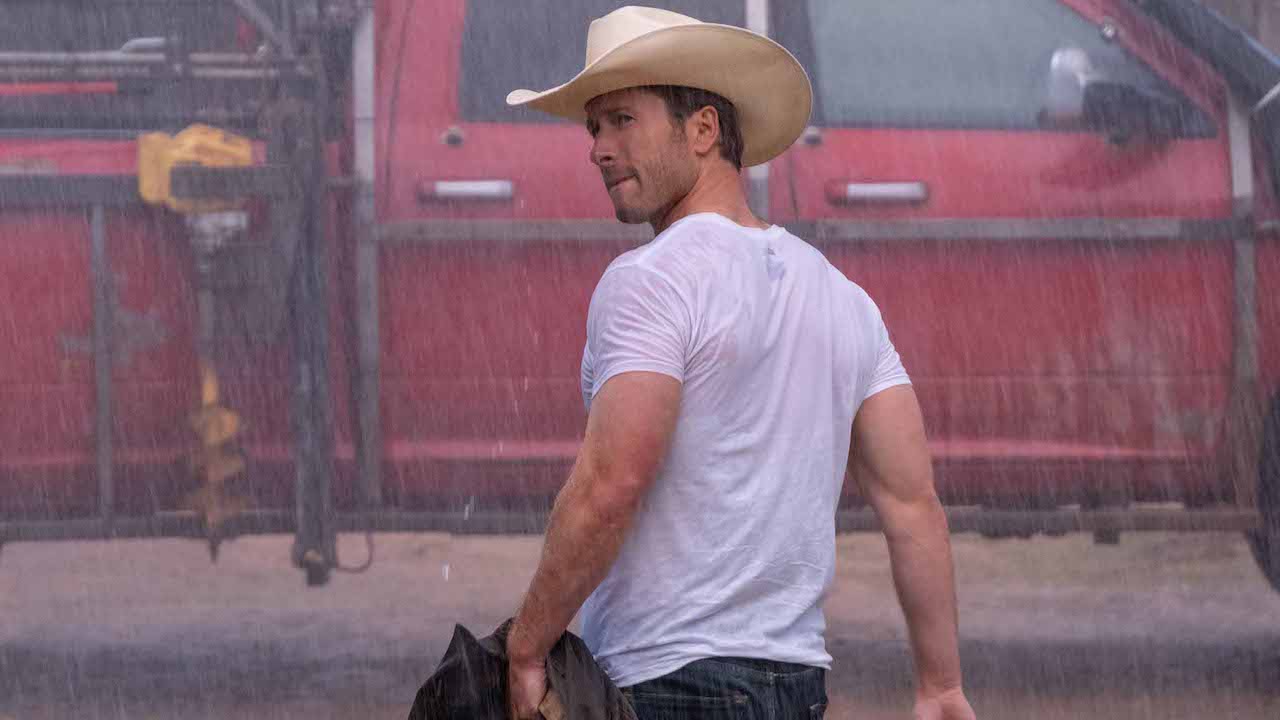 Glen Powell con una camiseta blanca bajo la lluvia en Twisters