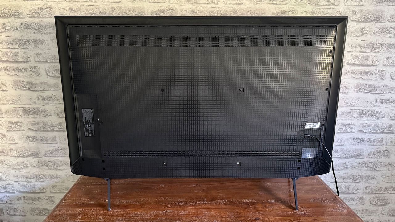The back of the TCL C6KS 50-inch TV in front of a brick wall, seen straight-on.